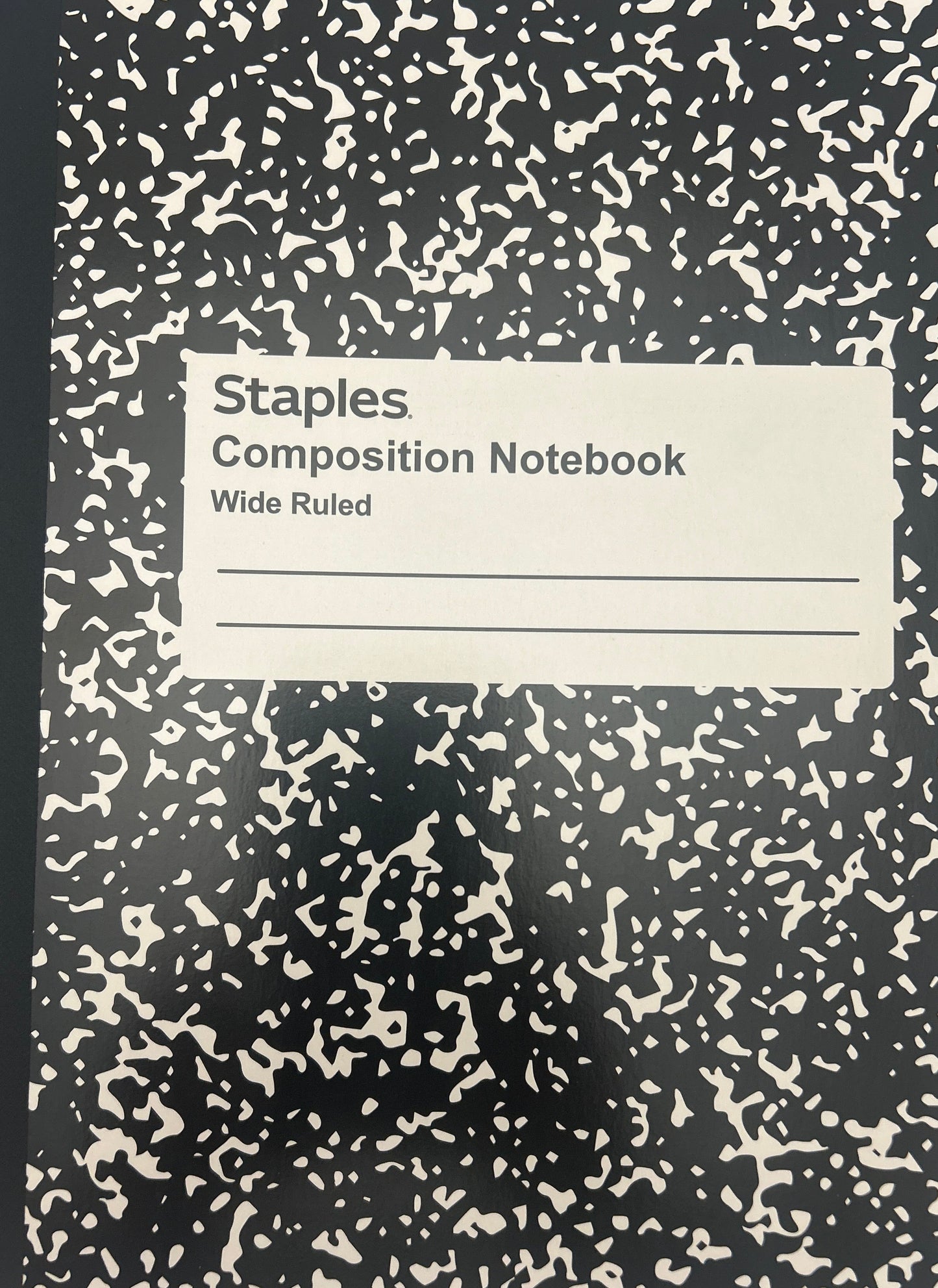 Black composition notebook with white speckled pattern on a light gray background