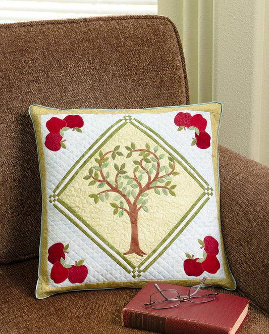 Decorative pillow with tree and apples design on a brown couch