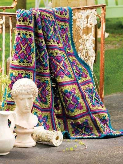 Colorful crocheted blanket draped over a decorative chair with classical sculpture and vase in the foreground.