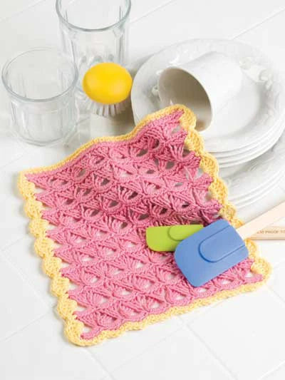 Pink crocheted dishcloth with cleaning tools on a white surface