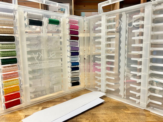 A clear plastic storage case containing 27 spools of Sulky 40 wt. Rayon embroidery thread in various colors and two spools of black and white bobbin thread. The product shown is a Sulky Embroidery Slimline Starter Pack.