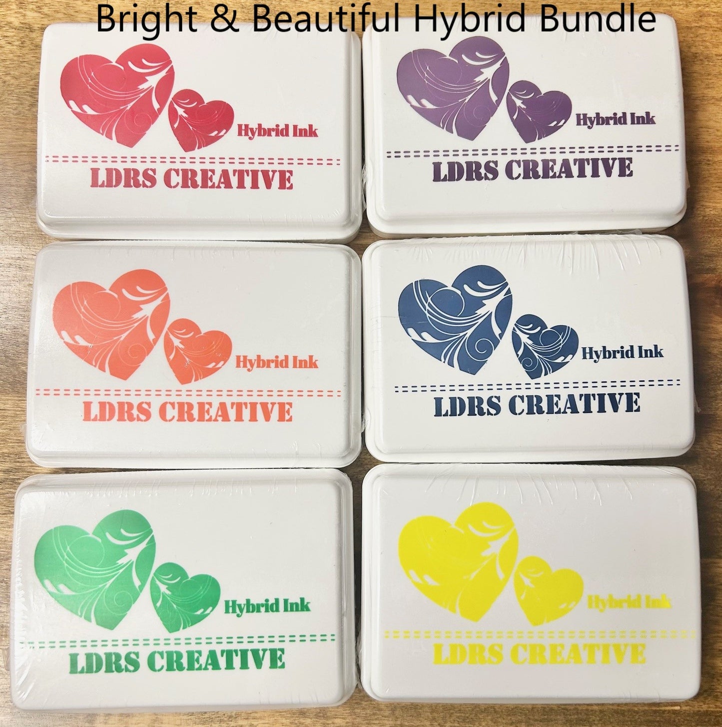 A high-quality description of six LDRS Creative Hybrid Ink pads from the "Bright & Beautiful" color set. The square, white ink pads feature a raised felt surface and include the colors: Kiss Me Red, Grape Ape, In Your Face Orange, Dark Wash Jeans, Four Leaf, and Lantern Yellow.