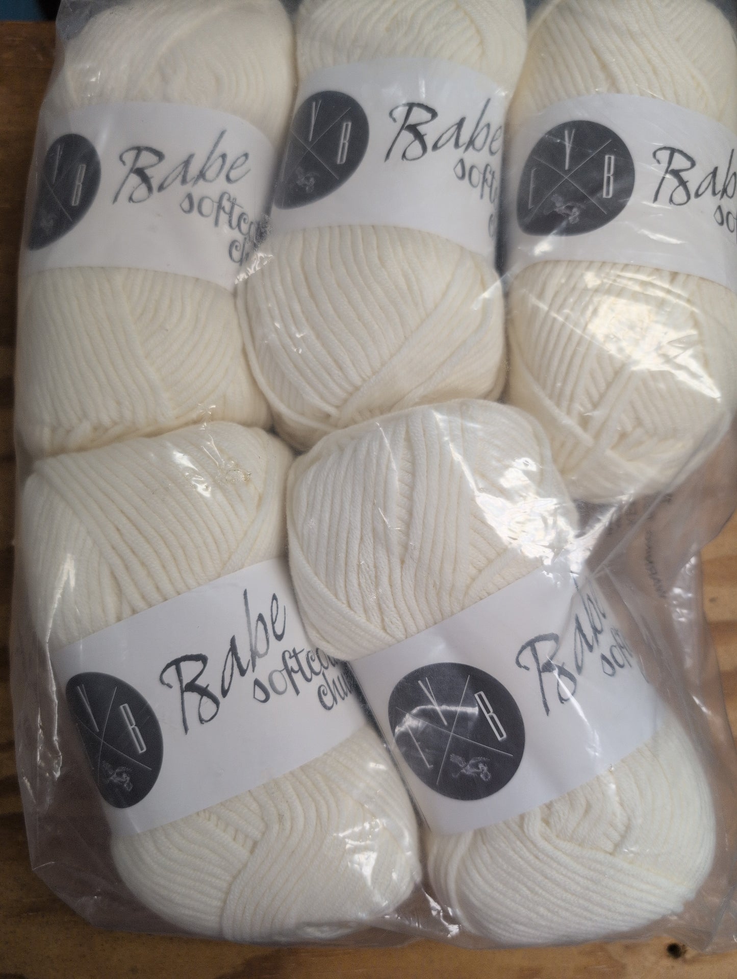 White yarn balls in clear packaging with visible labels on a wooden surface