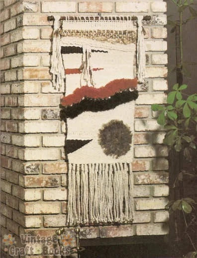 Woven textile art piece on a brick wall with 'Vintage Craft Books' branding.