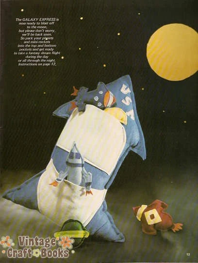 Illustration of a child's pillow with space-themed design, featuring a rocket and astronaut, against a night sky with moon.