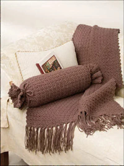 Brown knitted throw blanket with fringes draped over a white sofa.