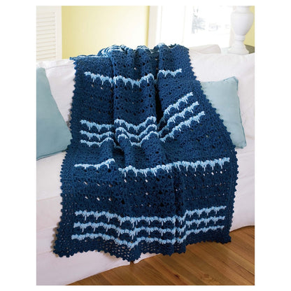 Blue and white crocheted blanket on a bed with pillows