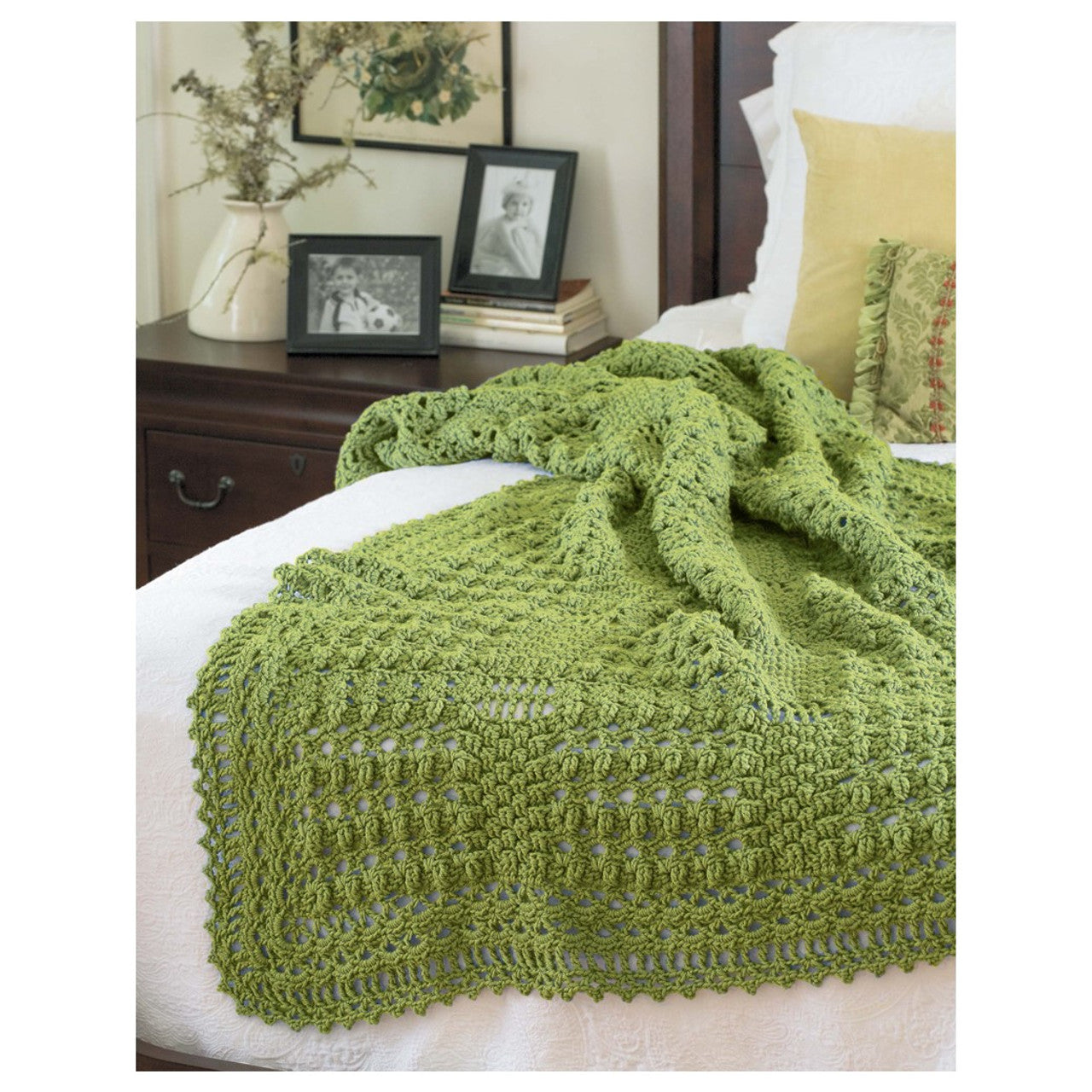Green crocheted blanket on a bed with a wooden nightstand and decor items.