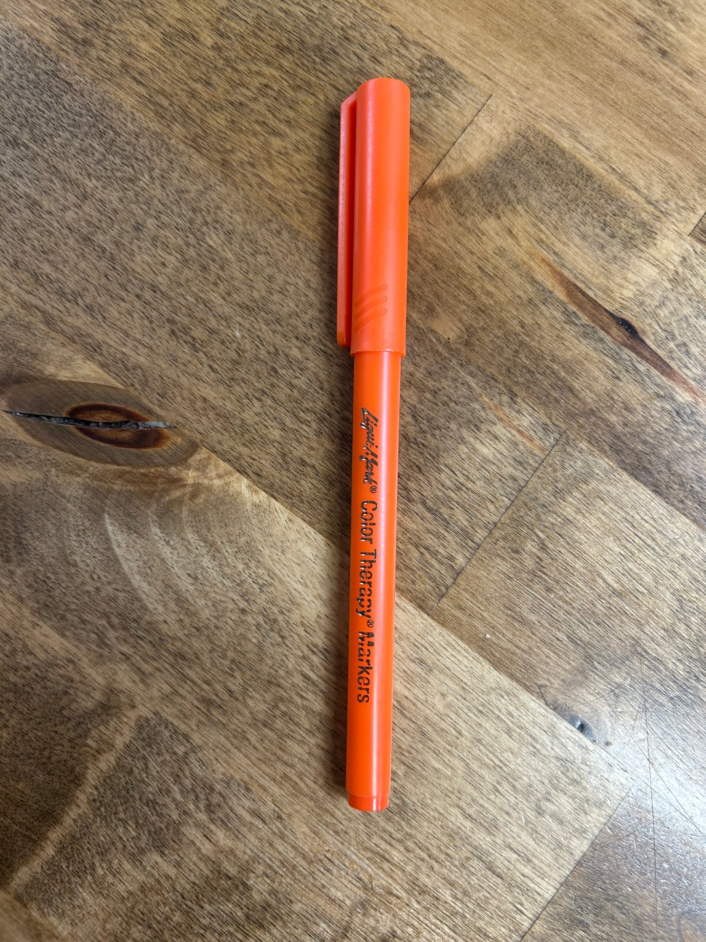 Orange marker labeled 'Color Therapy Markers' on a wooden surface