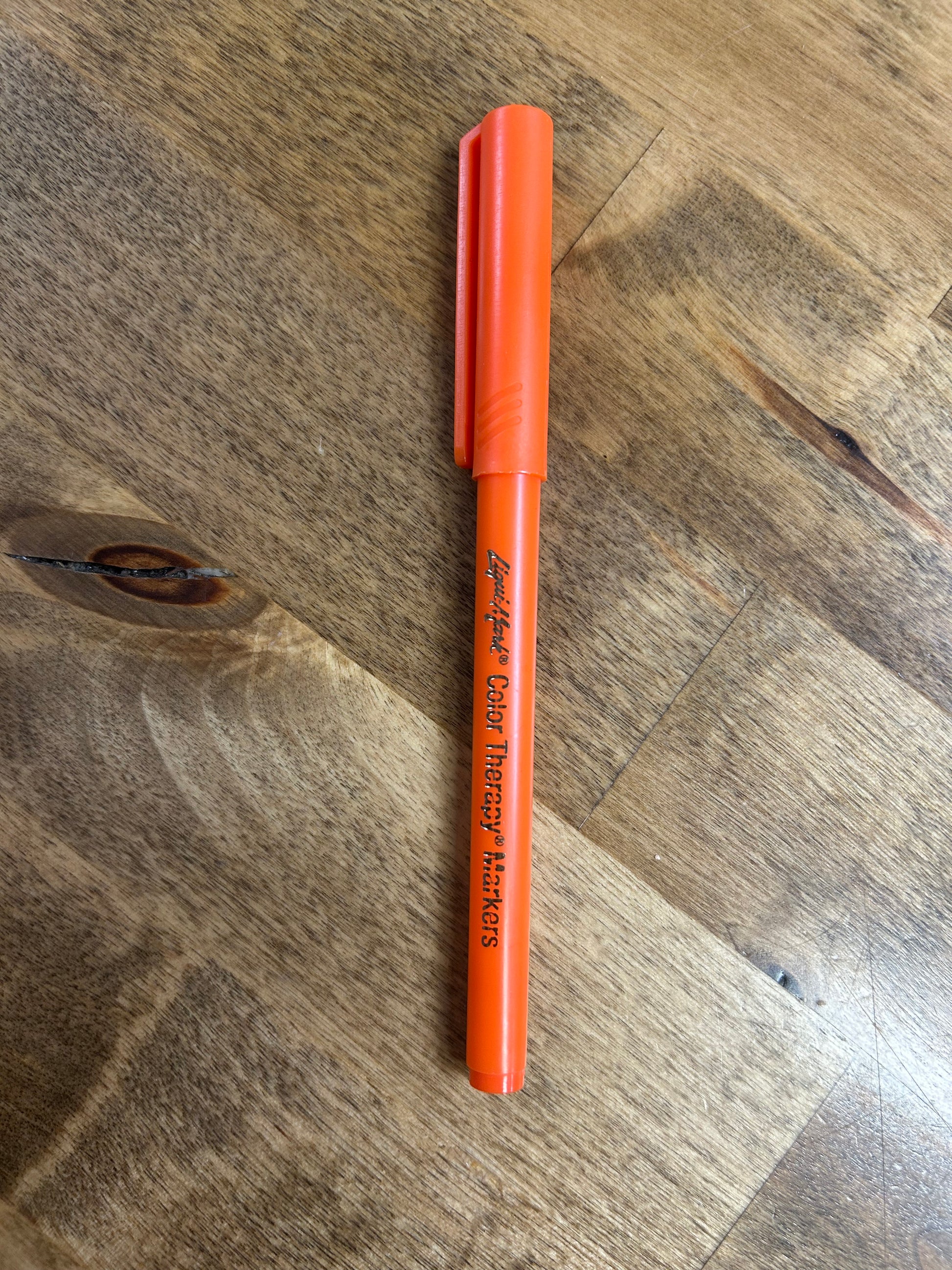 Orange marker labeled 'Color Therapy Markers' on a wooden surface