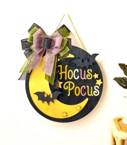 Halloween decorative sign with 'Hocus Pocus' text on a moon and bat design, featuring a bow.