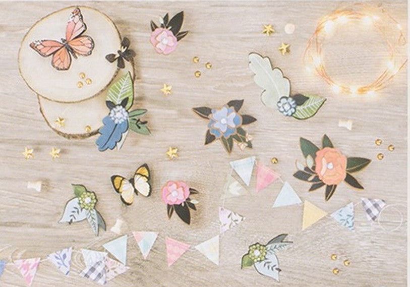 Decorative paper cutouts of flowers, butterflies, and stars on a wooden surface with string lights.