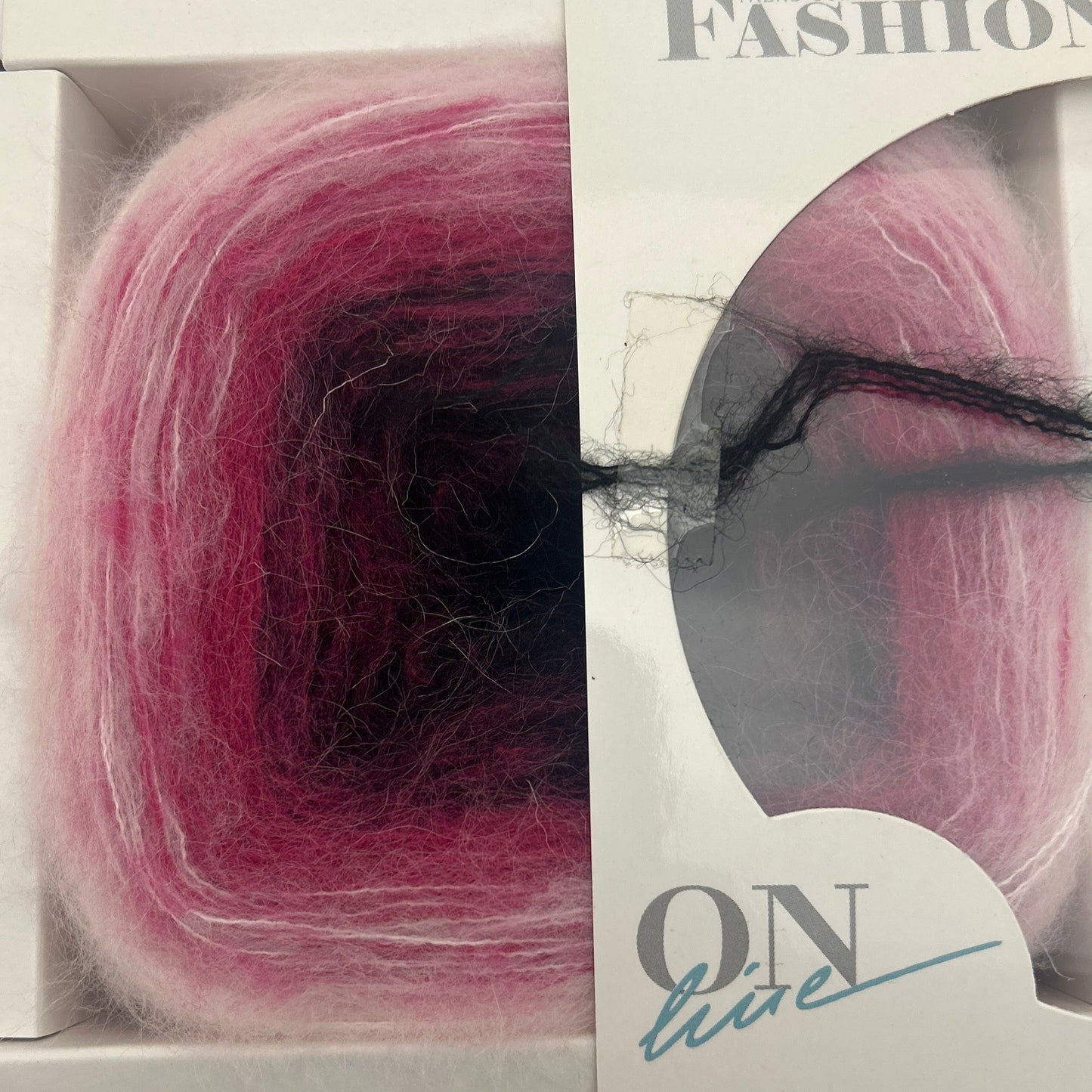 Yarn ball with a black thread through it, displayed in a clear packaging with visible brand name.