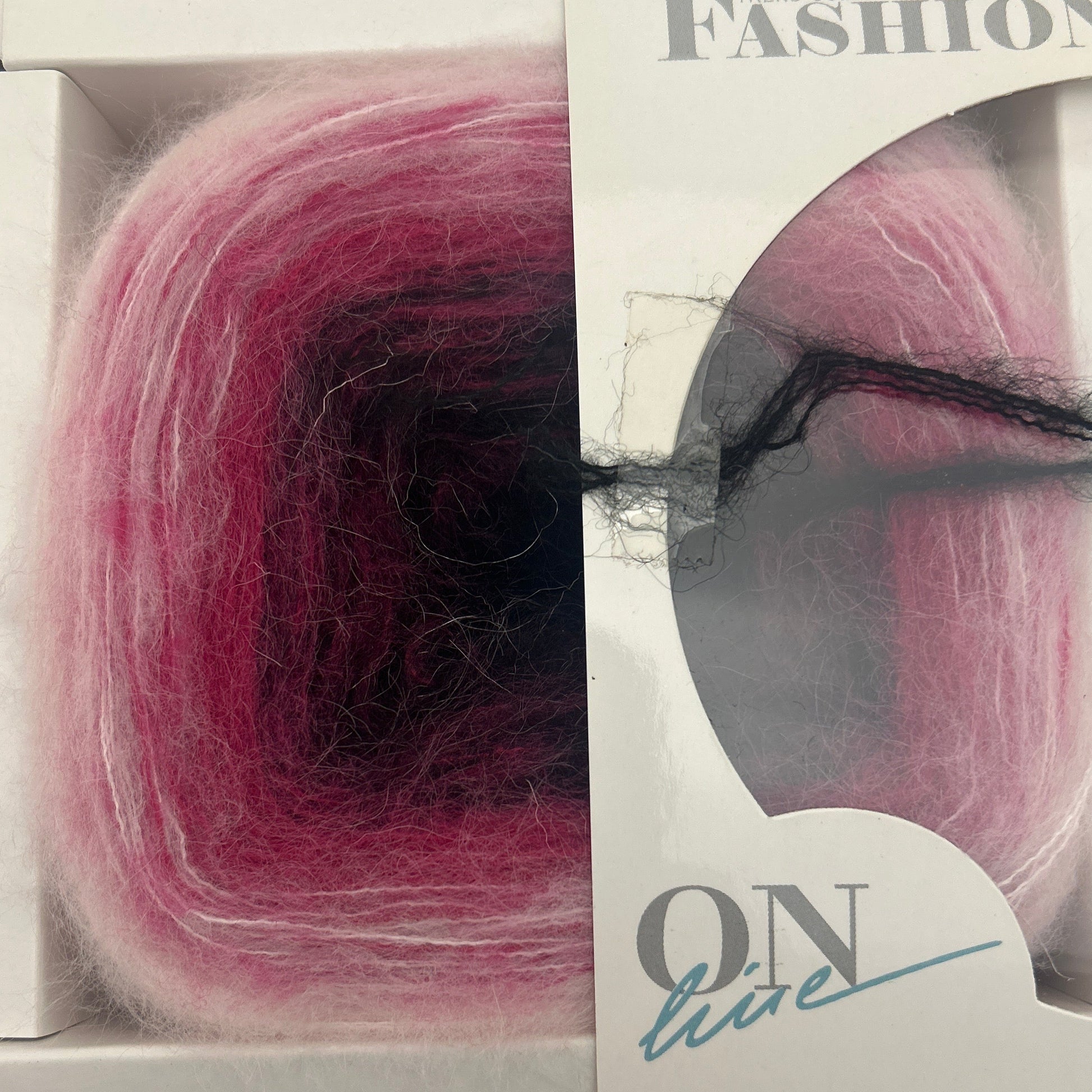 Yarn ball with a black thread through it, displayed in a clear packaging with visible brand name.