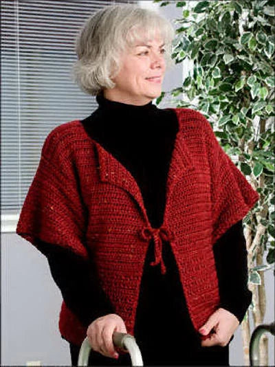 Woman wearing a red crocheted poncho in an indoor setting with plants.