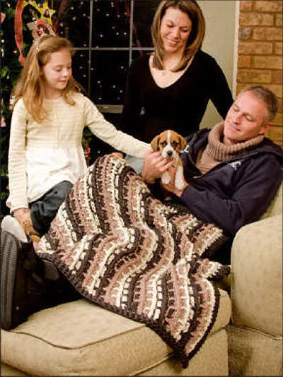 Family sitting on a couch with a dog, wrapped in a patterned blanket.