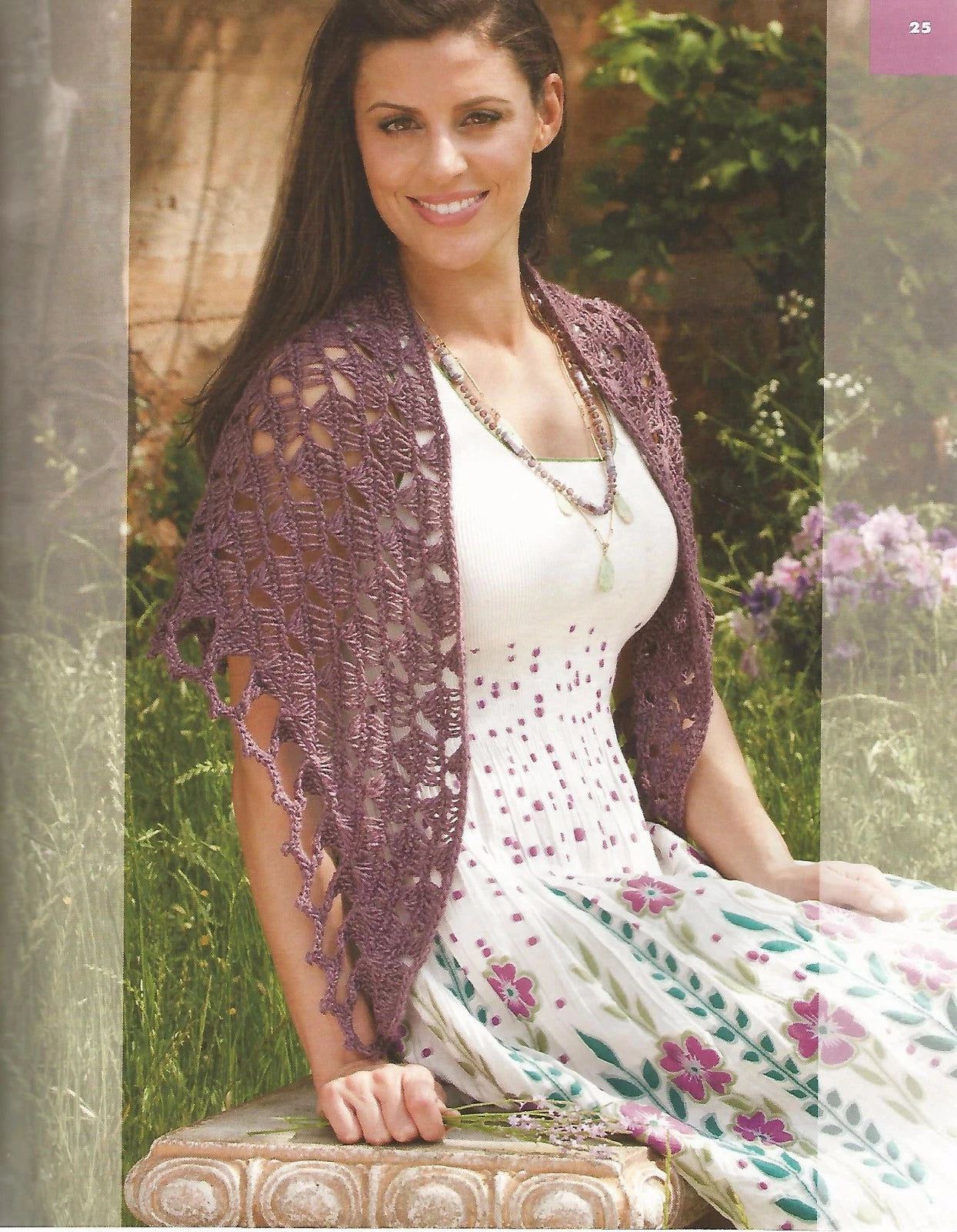 Woman wearing a purple knitted shawl sitting outdoors with flowers in the background