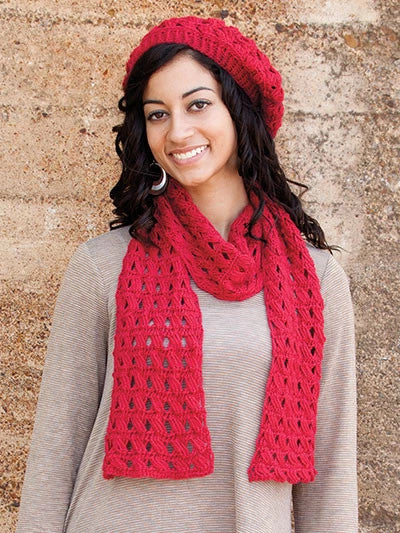Woman wearing a red knitted scarf and hat against a stone wall.