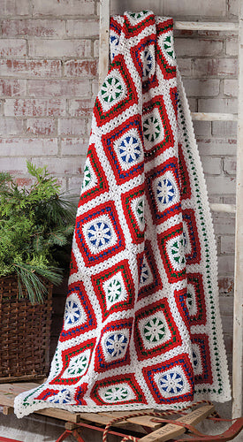 Crocheted blanket with geometric pattern draped over a wooden ladder against a brick wall.