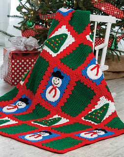 Colorful crocheted blanket with Christmas patterns on a wooden floor.