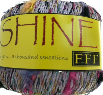 Multicolored yarn ball with a yellow label featuring the word 'SHINE' and branding.