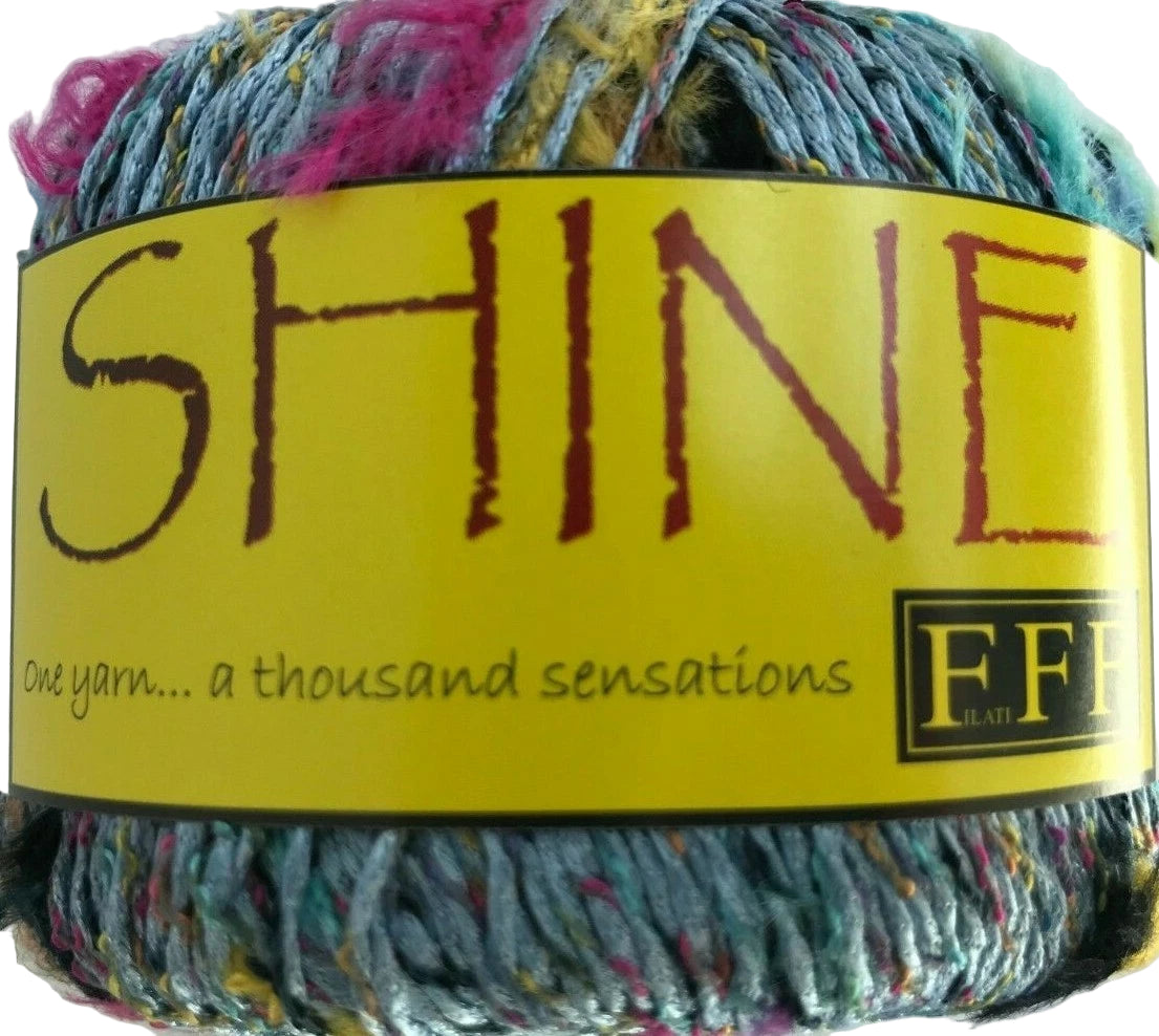 Multicolored yarn ball with a yellow label featuring the word 'SHINE' and branding details.