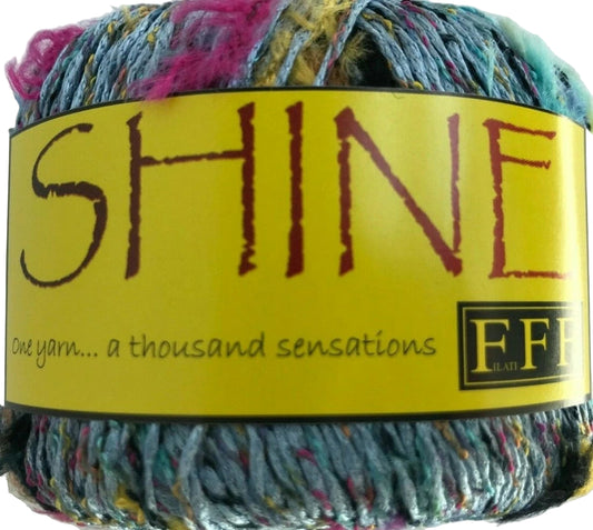 Multicolored yarn ball with a yellow label featuring the word 'SHINE' and branding details.