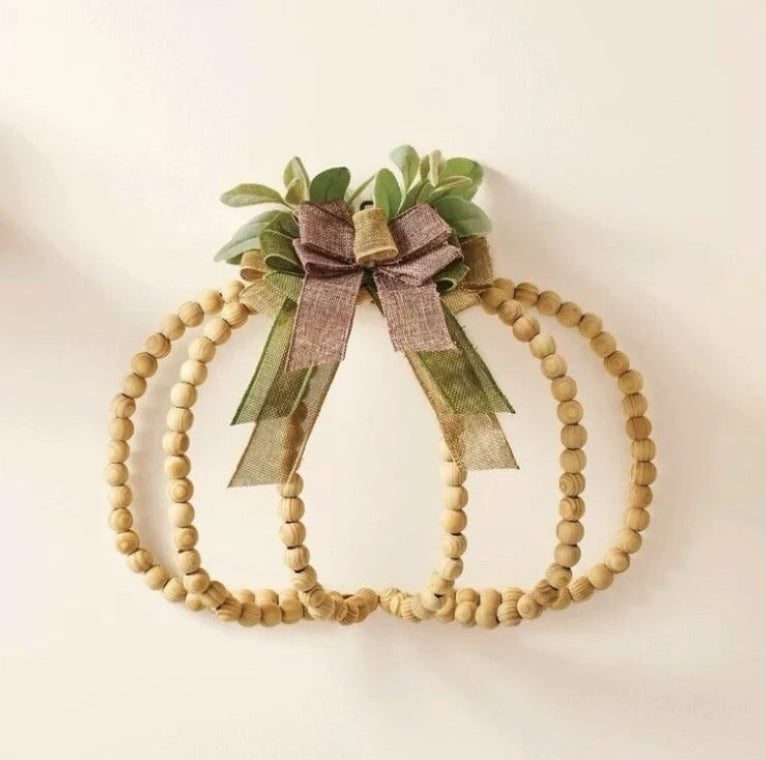 Wooden beaded pumpkins with a bow and greenery on a light background