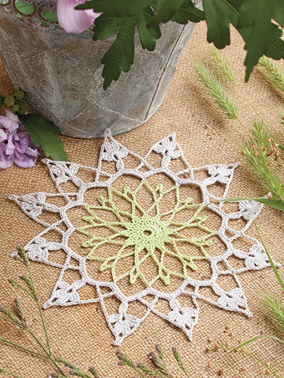 Crocheted doily with a green center on a textured surface with flowers and leaves.