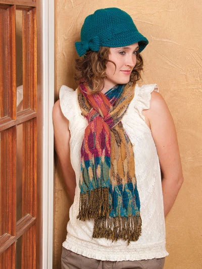 Woman wearing a blue knitted hat and colorful scarf against a beige wall.