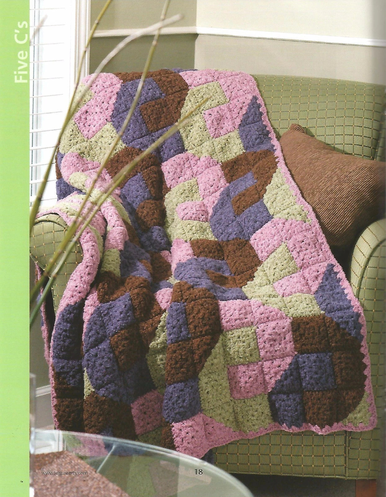 Colorful crocheted blanket on a green couch with a window in the background