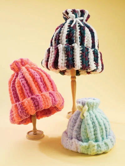 Three colorful knitted hats on mannequin stands against a yellow background