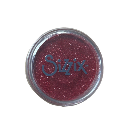 Small container of glitter with 'Sizzix' branding on a beige background