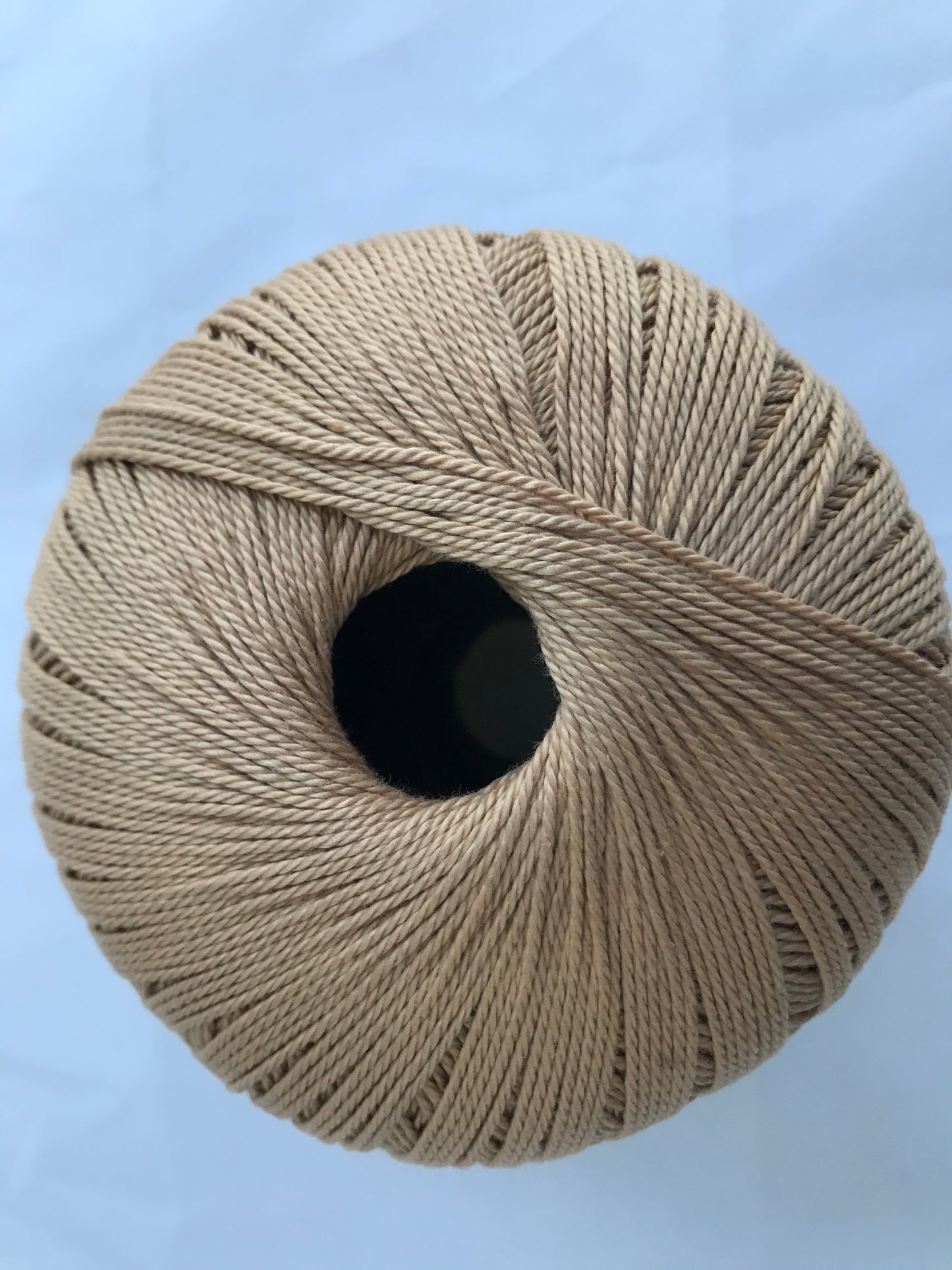 Ball of beige yarn on a light blue background
