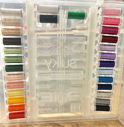 A clear plastic storage case containing 27 spools of Sulky 40 wt. Rayon embroidery thread in various colors and two spools of black and white bobbin thread. The product shown is a Sulky Embroidery Slimline Starter Pack. 