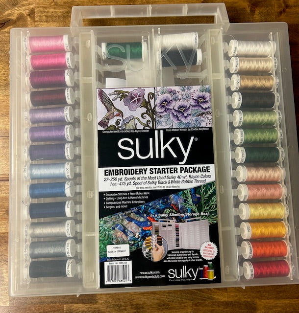 A clear plastic storage case containing 27 spools of Sulky 40 wt. Rayon embroidery thread in various colors and two spools of black and white bobbin thread. 