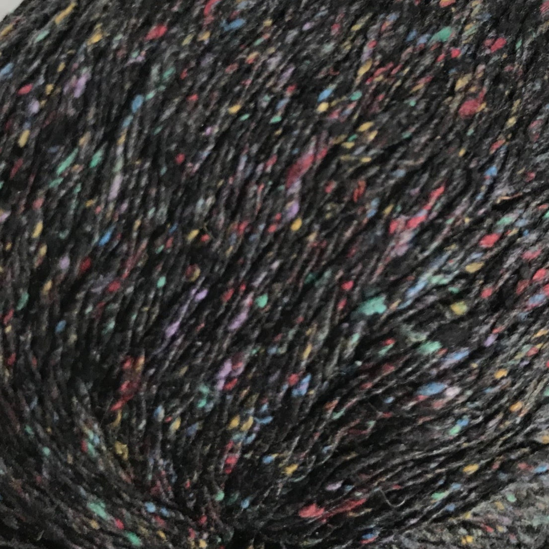 Close-up of speckled yarn ball with multicolor specks on a black background