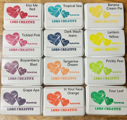 Nine LDRS Creative Hybrid Ink pads in various colors, arranged in three rows. The colors visible include Kiss Me Red, Tropical Sea, Banana Cream Pie, Tickled Pink, Dark Wash Jeans, Lantern Yellow, Boysenberry Blast, Tangerine Dream, Prickly Pear, Grape Ape, In Your Face Orange, and Four Leaf. This alt text is useful for accessibility purposes and for search engines to index the image appropriately based on its content and context on the page.