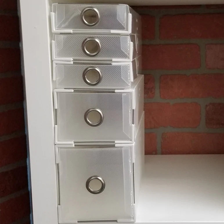 Stack of clear plastic drawers with metallic knobs against a brick wall.