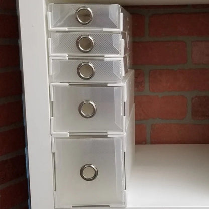 Stack of clear plastic drawers with metallic knobs against a brick wall.