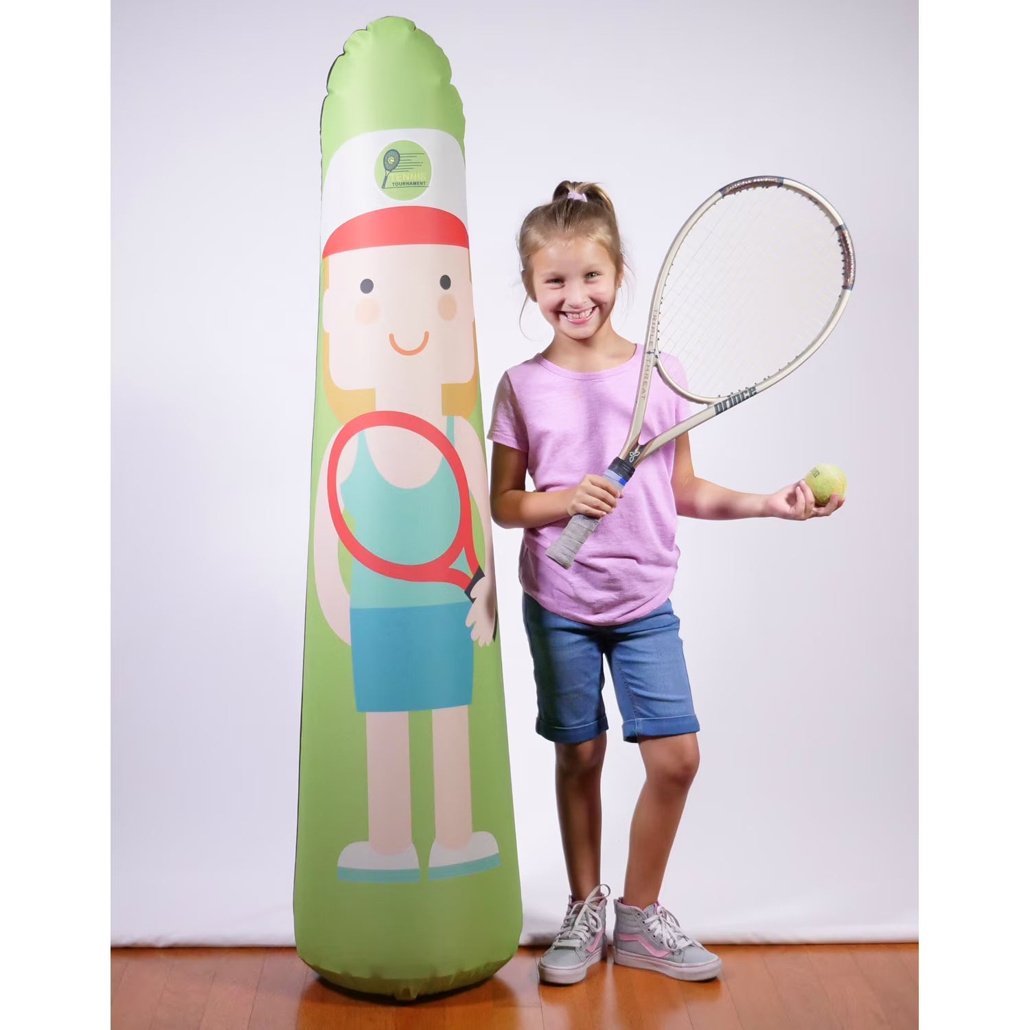 Child holding a tennis racket and ball next to an inflatable tennis player on a white background