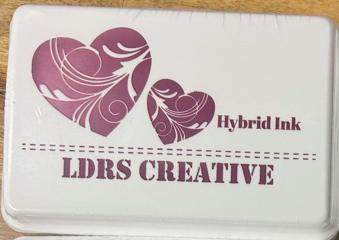 An image of a white ink pad featuring two purple hearts and the text "LDRS CREATIVE Hybrid Ink" in a bright purple color.