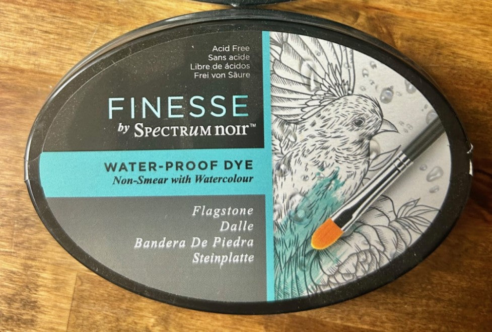 A round, dark grey Crafter's Companion Spectrum Noir Finesse water-proof dye ink pad in the color "Flagstone". The ink pad is acid-free and designed for use with watercolour media as it is water-proof.