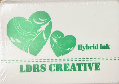 An image of a white ink pad featuring two green hearts with white decorative swirls and the text "LDRS CREATIVE Hybrid Ink" and the color name "Four Leaf" in green.
