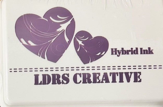 An image of a white ink pad featuring two purple colored hearts with white decorative swirls and the text "LDRS CREATIVE Hybrid Ink" in purple.