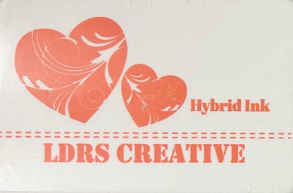 An image of a white ink pad featuring two orange-colored hearts with white decorative swirls and the text "LDRS CREATIVE Hybrid Ink" and the color name "In Your Face Orange" in orange.