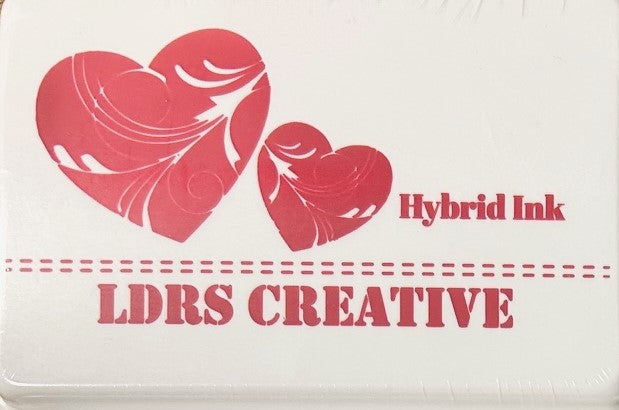 An image of a white ink pad featuring two red hearts with white decorative swirls and the text "LDRS CREATIVE Hybrid Ink" and the color name "Kiss Me Red" in red. 