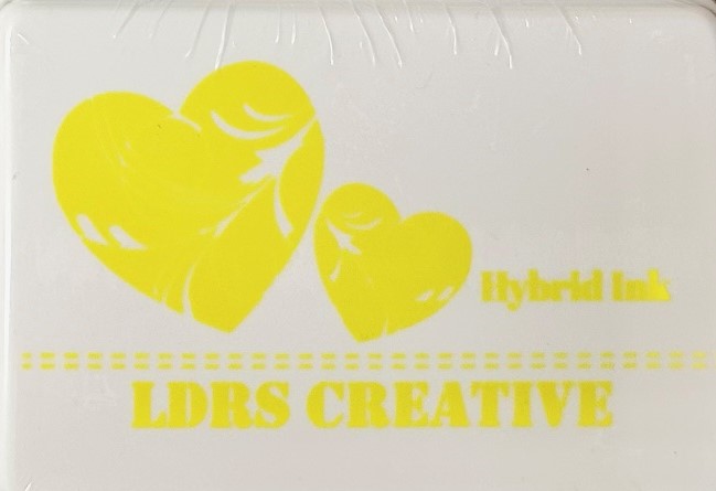An image of a white ink pad featuring two yellow hearts with white decorative swirls and the text "LDRS CREATIVE Hybrid Ink" and the color name "Lantern Yellow" in yellow.