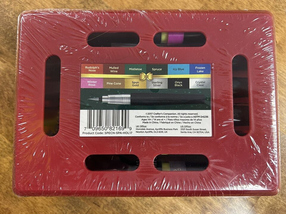 A red packaging of Spectrum Noir Sparkle Brush Markers Holiday 12 pc Set. Rudolphs Nose Red, Mulled Wine, Mistletoe, Spruce, Icy Blue, Frozen Lake, Winter Rose, Pine Cone, Spun Gold, Sterling Silver, Onyx Black, Crystal Clear