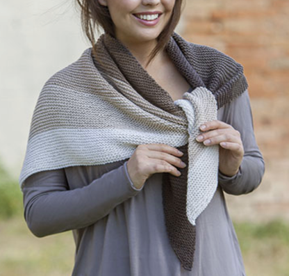 Woman wearing a knitted shawl with a gradient of colors against a blurred outdoor background